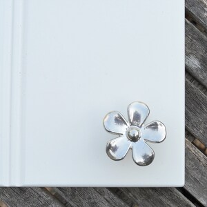 May include: Silver flower-shaped cabinet knob with a raised centre.