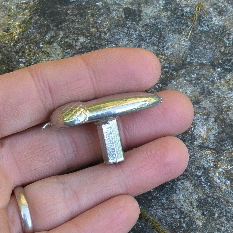 May include: A silver metal T-shaped knob with a textured top. The knob has a square shaft.