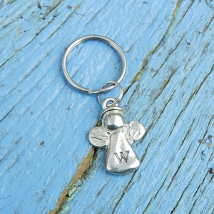 Peut inclure: Porte-clés argenté en forme d'ange avec la lettre "W" gravée sur le devant. L'ange a des ailes et une auréole, attaché à un anneau métallique. Le fond est une surface en bois bleu clair vieilli.