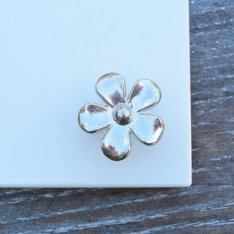 May include: Silver flower-shaped cabinet knob with a raised centre.
