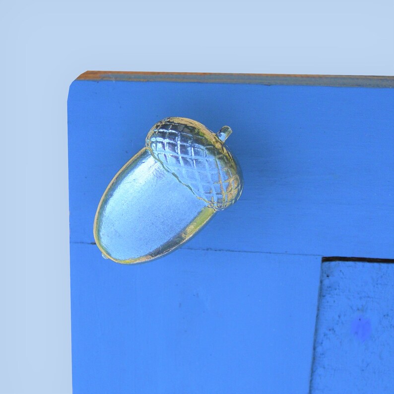 May include: A silver acorn shaped door knob with a textured design. The knob is mounted on a light blue wooden surface.