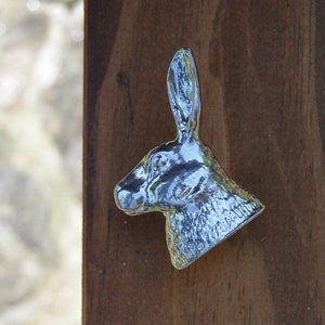 Peut inclure: Une décoration murale en métal argenté en forme de tête de lapin. Le lapin a un long nez pointu et de grandes oreilles. Le lapin est tourné vers la droite.