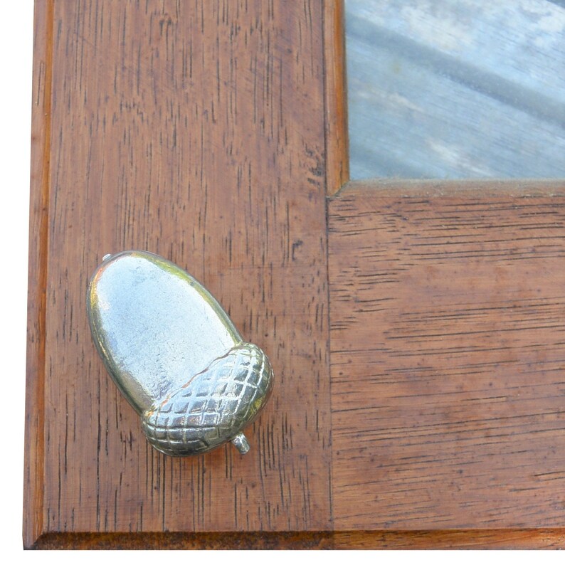 May include: A silver acorn shaped door knob or pull, mounted on a wooden surface.