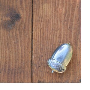 May include: A silver acorn ornament on a wooden background.