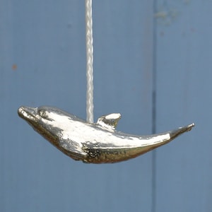 Pode incluir: Uma corrente de puxar de luz de prata em forma de golfinho. O golfinho está suspenso por um cordão branco.