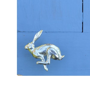 May include: A silver rabbit figurine in a leaping pose, mounted on a light blue wall.
