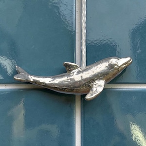 Tirante per luce a forma di delfino che salta, in peltro fuso a mano, finitura lucida.