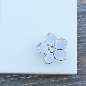 May include: A silver flower-shaped cabinet knob with a five-petal design. The knob has a raised centre with a smaller flower design.