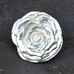 Peut inclure: Un pendentif en argent en forme de rose avec un design texturé détaillé. Le pendentif est en métal et a une finition brillante.