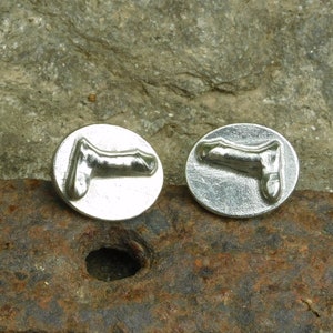 May include: A pair of silver cufflinks featuring a raised design of a human body part. The cufflinks are round and have a smooth surface.
