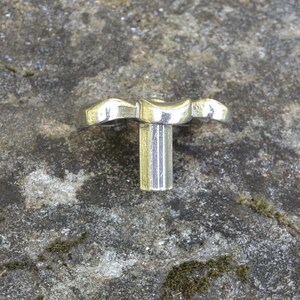 May include: A silver metal knob with a decorative, wavy design. The knob has a cylindrical stem.