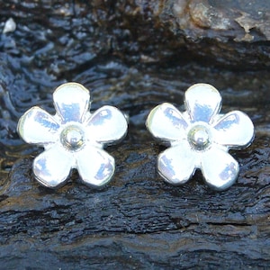 May include: A pair of silver flower stud earrings. The earrings are small and delicate, with a simple design. They are perfect for everyday wear.