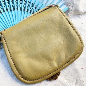 May include: A small, olive green leather purse with a fringe tassel. The purse has a simple design and a braided strap.