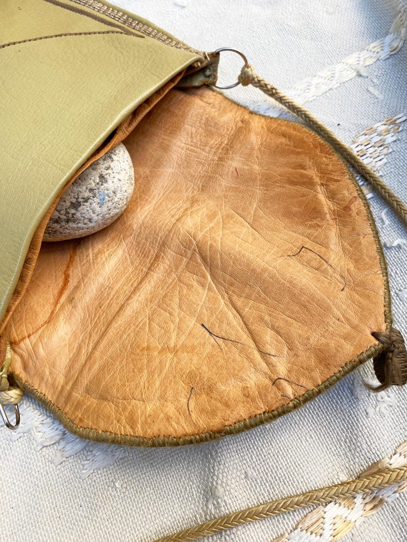 May include: A green leather bag with a brown leather lining. The bag has a long strap and a small pocket on the front.