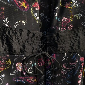 Puede incluir: Un vestido negro con estampado floral y un lazo de cinta de sat&eacute;n negro en la cintura.