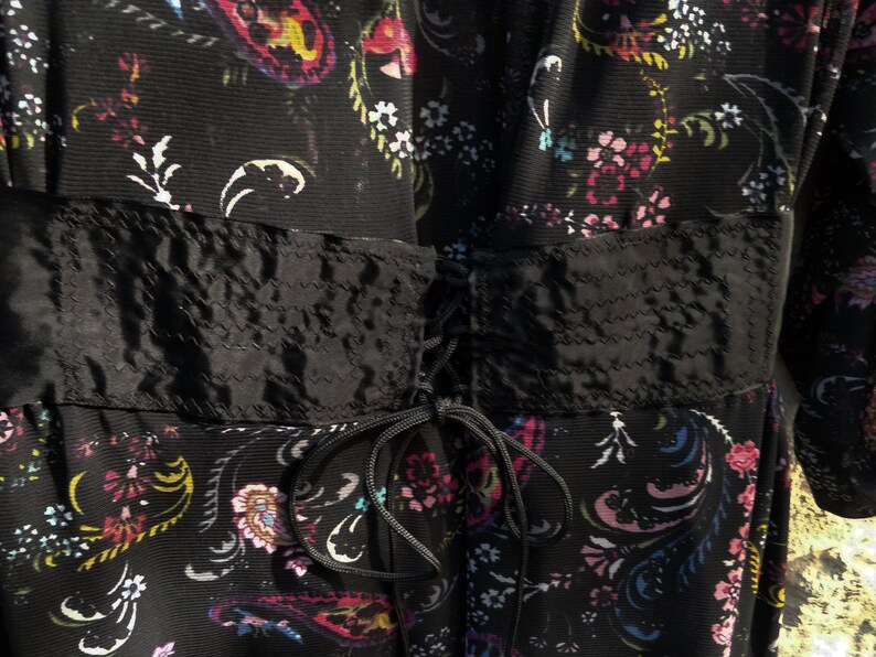Puede incluir: Un vestido negro con estampado floral y un lazo de cinta de sat&eacute;n negro en la cintura.