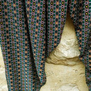 May include: Green fabric with a repeating pattern of white, green, yellow, and brown circles. The fabric is folded in half and draped over a stone wall.