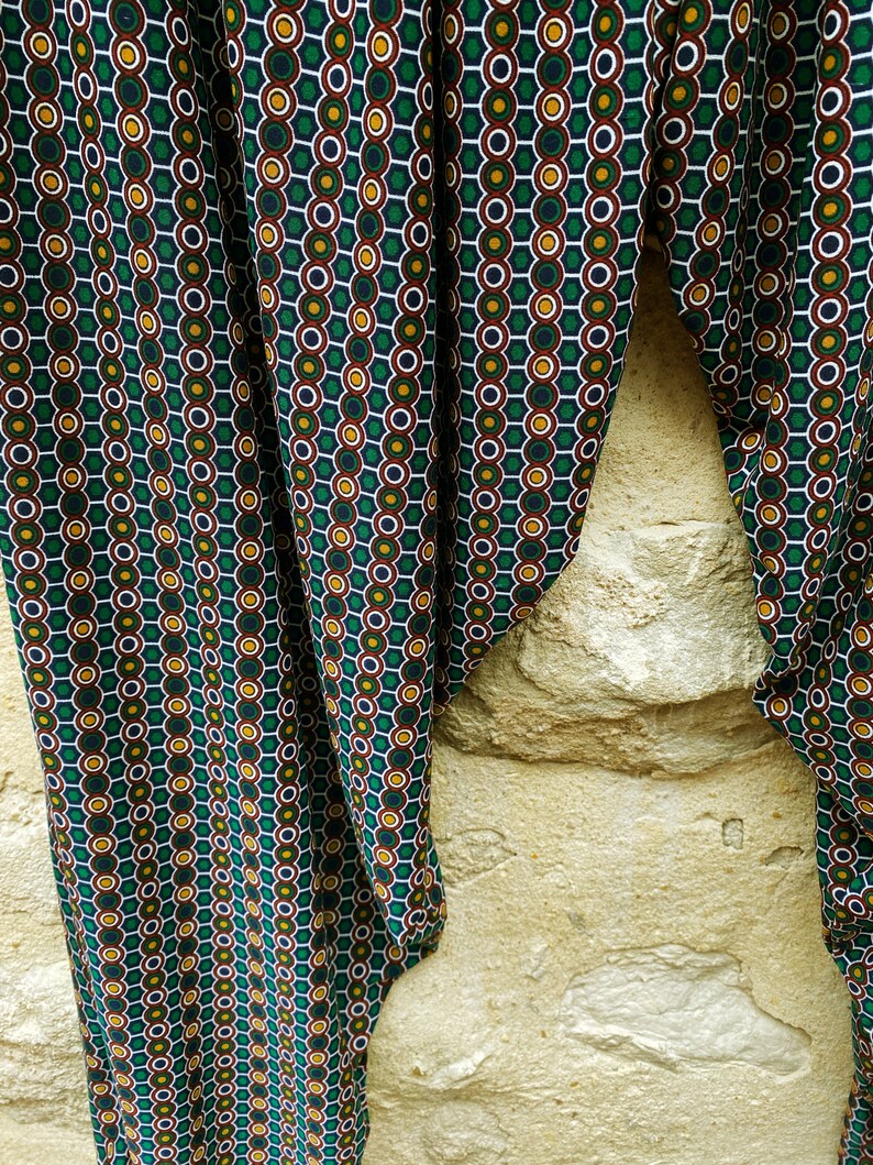 May include: Green fabric with a repeating pattern of white, green, yellow, and brown circles. The fabric is folded in half and draped over a stone wall.