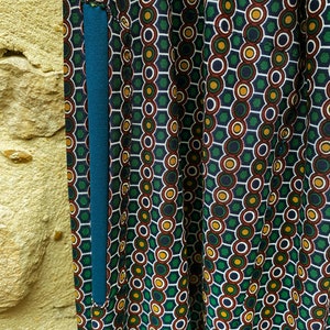 May include: Close-up of a teal blue fabric pocket sewn onto a green, red, white, and yellow patterned fabric. The pattern is made up of circles and hexagons.