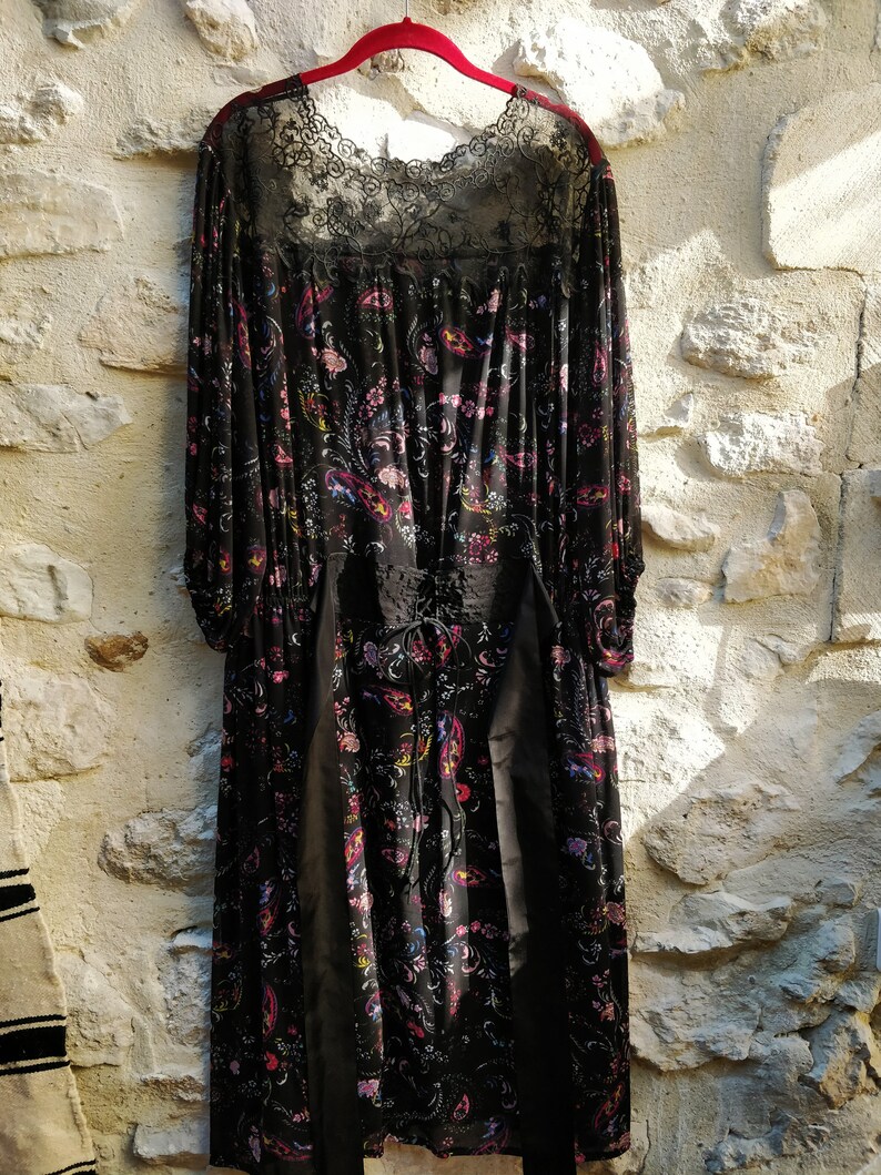 Puede incluir: Un vestido maxi negro con estampado floral y escote de encaje. El vestido tiene mangas largas y un corpi&ntilde;o ajustado.