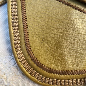May include: Close-up of a mustard yellow leather bag with a brown braided trim around the edge.