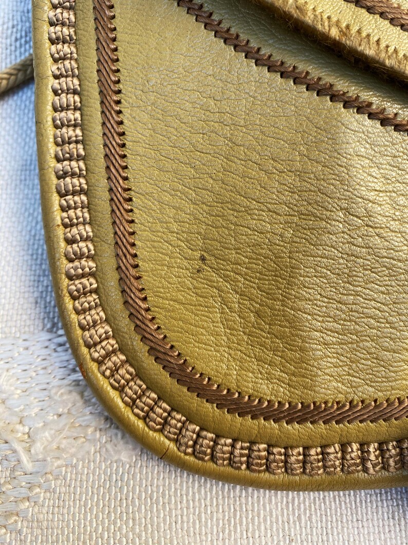 May include: Close-up of a mustard yellow leather bag with a brown braided trim around the edge.