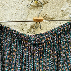 May include: A green, brown, and white patterned skirt with a gathered waistband hangs on a silver hanger.
