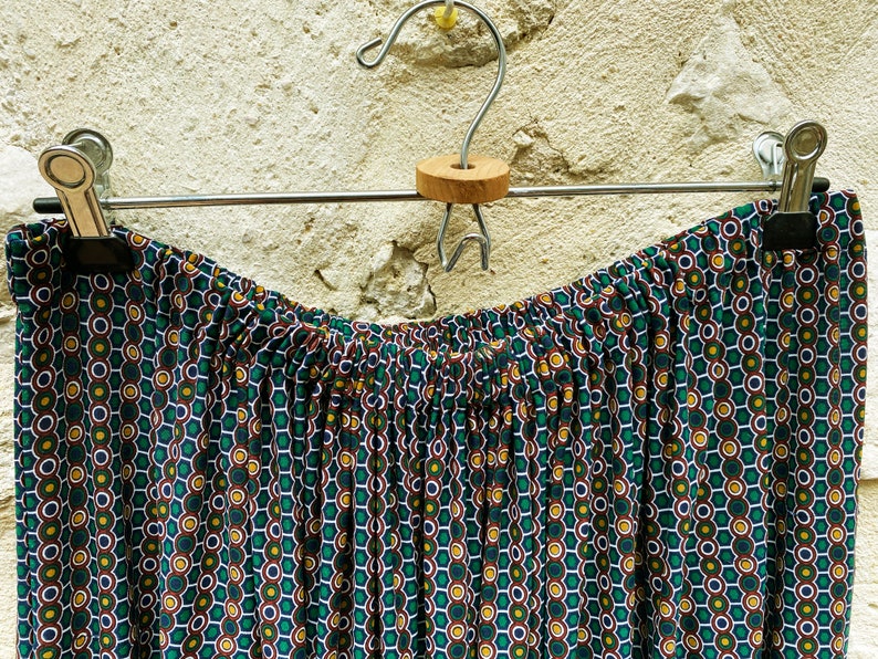 May include: A green, brown, and white patterned skirt with a gathered waistband hangs on a silver hanger.