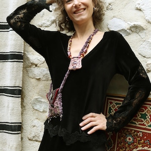 May include: A woman wearing a black velvet dress with lace trim and a long, beaded necklace with a purple pendant. The necklace is made of beads and has a tassel at the end.