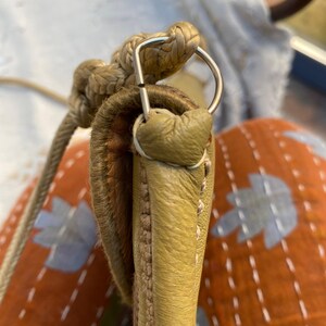 May include: Close-up of a light green leather handbag with a braided rope strap and a silver metal loop.