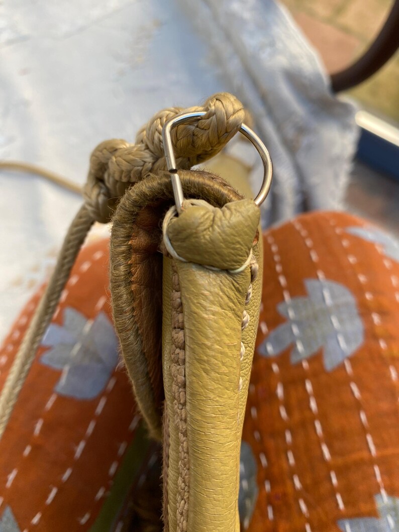 May include: Close-up of a light green leather handbag with a braided rope strap and a silver metal loop.
