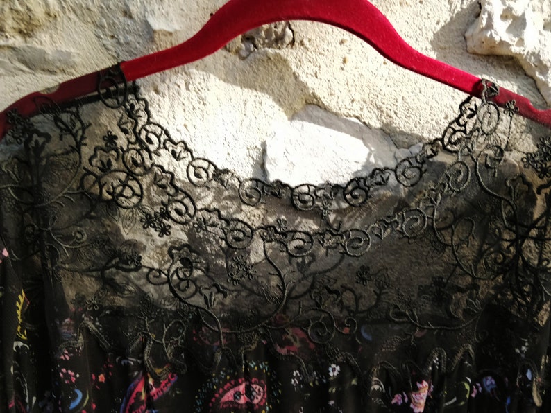 Puede incluir: Borde de encaje negro con un patr&oacute;n floral sobre un fondo de tela negro. El encaje es delicado e intrincado, con un borde festoneado.
