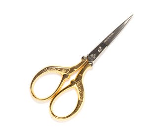 May include: Gold-colored decorative scissors with a silver blade. The scissors have an ornate design on the handles.