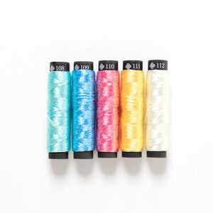 May include: Five spools of embroidery floss in different colors: light blue, blue, pink, yellow, and white. The spools are labeled with numbers 108, 109, 110, 111, and 112.
