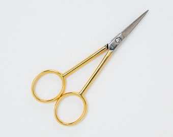 May include: Gold-colored small scissors with silver blades. The scissors have a classic design with rounded handles.