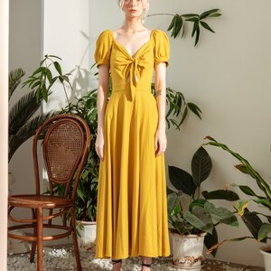 May include: A yellow maxi dress with a tie at the neckline and puff sleeves. The dress is made of a lightweight fabric and has a flowy silhouette.
