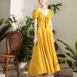 May include: A yellow maxi dress with a tie at the waist and puff sleeves. The dress is made of a lightweight fabric and has a flowy silhouette.