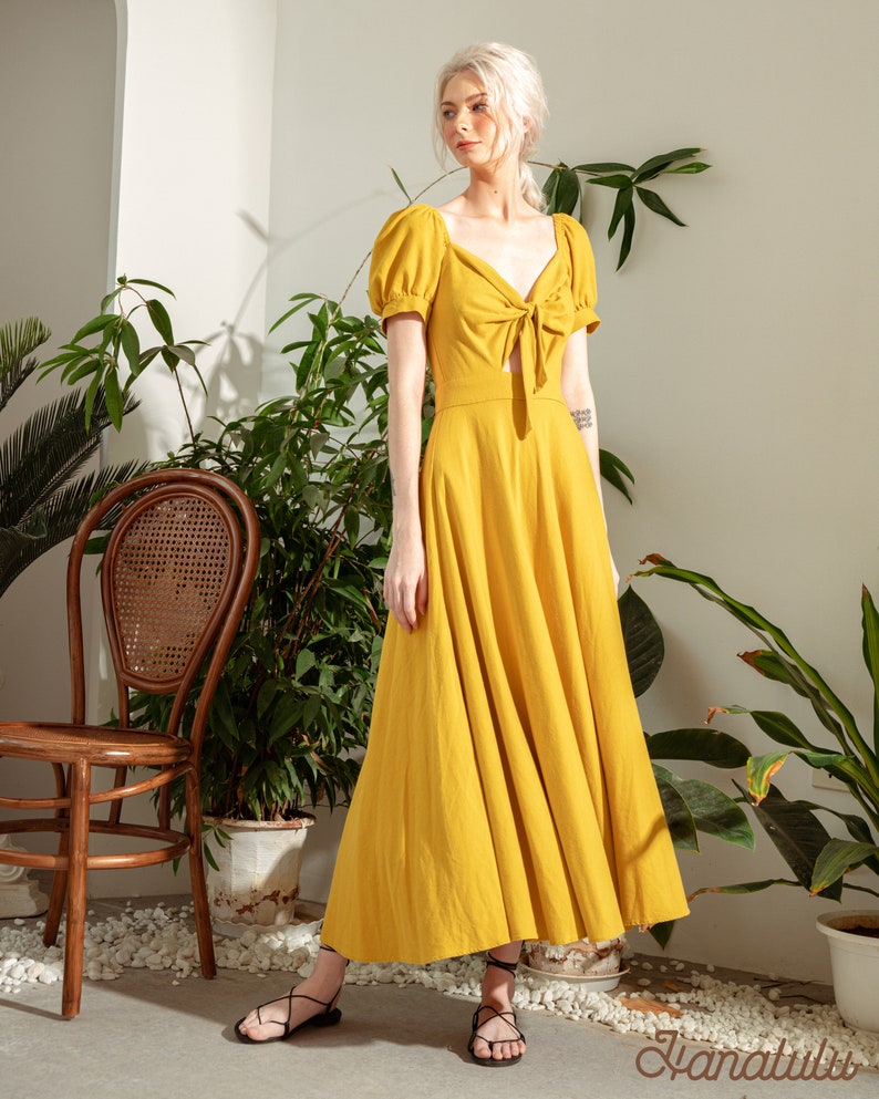 May include: A yellow maxi dress with a tie at the waist and puff sleeves. The dress is made of a lightweight fabric and has a flowy silhouette.
