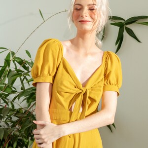 May include: A yellow linen dress with a tie at the neckline and short puff sleeves.