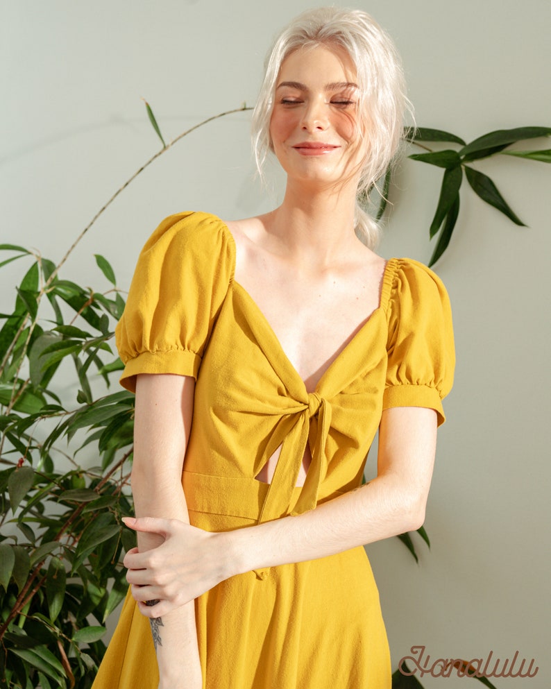 May include: A yellow linen dress with a tie at the neckline and short puff sleeves.