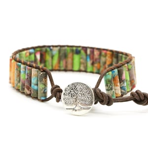 May include: A brown leather bracelet with a tree of life charm. The bracelet is made with colorful, multi-colored, and patterned beads.