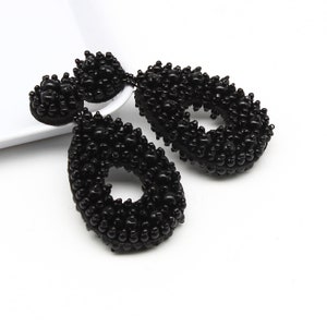 Puede incluir: Un par de pendientes negros en forma de lágrima hechos de pequeñas cuentas negras. Los pendientes tienen un gran agujero en el centro de cada lágrima.