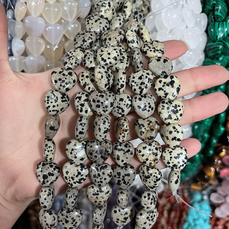 May include: A strand of heart-shaped dalmatian jasper beads. The beads are a light brown color with black spots.