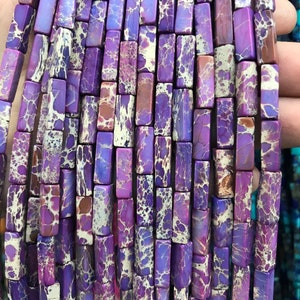May include: A strand of purple and white patterned rectangular gemstone beads. The beads are approximately 1/2 inch long and 1/4 inch wide.