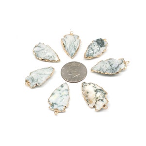 May include: Eight green and white agate arrowhead pendants with gold-plated edges. The pendants are arranged in a circle around a US quarter.