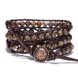 May include: A brown leather wrap bracelet with multiple strands of brown and white patterned beads and a copper button closure.