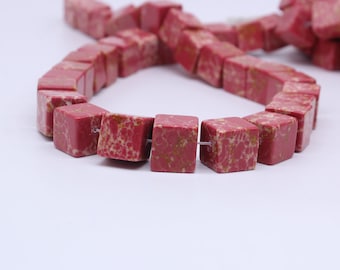 May include: A strand of red and white speckled square beads. The beads are made of natural stone and are strung on a white thread.