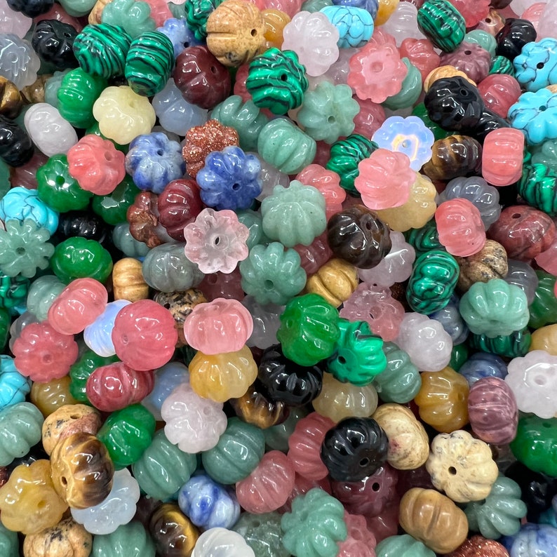 May include: A large assortment of colorful gemstone beads, each carved into a unique flower shape. The beads are made from various types of stones, including green jade, pink rose quartz, blue lapis lazuli, and brown tiger's eye.