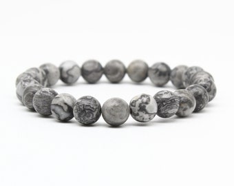 May include: A gray and white patterned beaded bracelet. The bracelet is made of round beads with a marbled pattern.