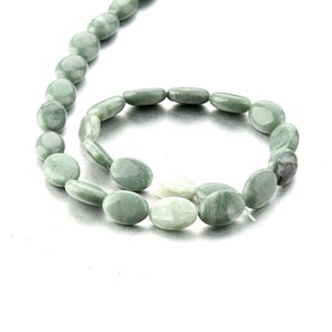 Puede incluir: Una hebra de cuentas de jade verde de forma ovalada. Las cuentas son lisas y pulidas, de color verde claro.